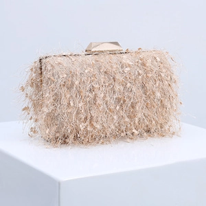 Detail view of beige fringe clutch bag with golden metallic clasp on white display cube