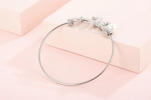 Detailed shot of a silver steel bangle featuring a white pearl and number five pendant