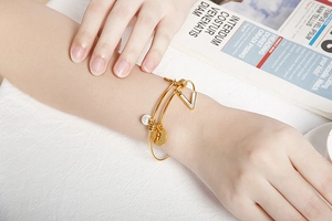 Macro detail of gold stainless steel bangle with shell V-pendant, pearl, and rabbit charm
