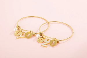Detail of gold titanium steel bracelets with shell letter charms and pearl accents