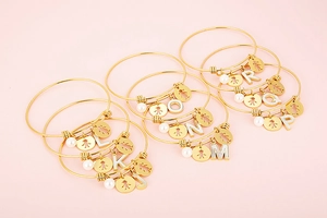 Detail of gold alphabet bracelets featuring shell charms and pearl pendants on pink base