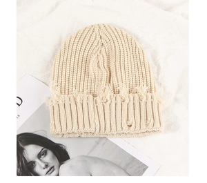 Détails de ce bonnet en maille beige avec bords déchirés et finitions effilochées