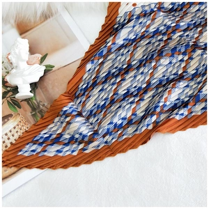 Close-up of pleated silk scarf with caramel and blue geometric patterns for women