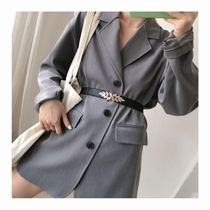 Detail of a thin black elastic belt with a golden leaf buckle on a grey dress for women