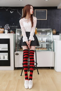 Detail of red and black striped over-knee socks worn with white shoes in a cafe setting