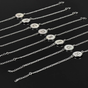 Bracelets en acier argenté avec breloques lettres A-H en nacre sur fond noir réfléchissant