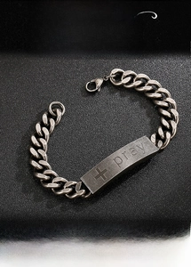 Macro detail of retro steel Cuban link bracelet with cross and Pray engraving