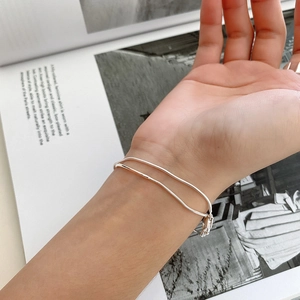 Close-up of minimalist double-layer silver snake chain bracelet worn on wrist over a magazine