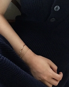Detail shot of minimalist gold snake chain bracelet on a model's wrist against dark knitwear