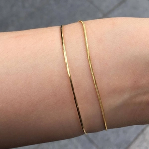Close-up of minimalist gold thin bangle and snake chain bracelet set worn on wrist