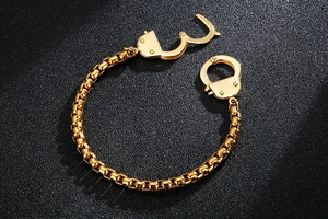 Detailed view of a gold geometric handcuff bracelet with square box chain on black surface