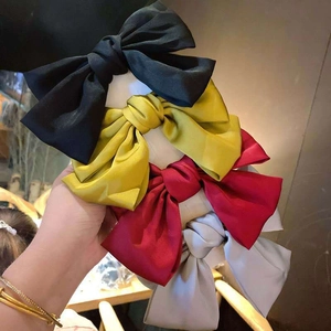 Close-up of four large satin bow hair clips in black, gold, wine red and silver grey