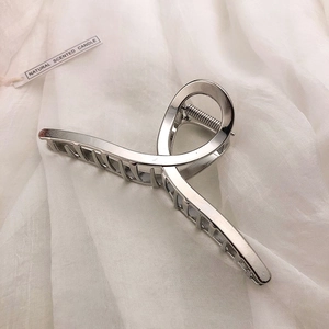 Detail of a minimalist silver metal hair claw clip with a twisted alloy design on fabric