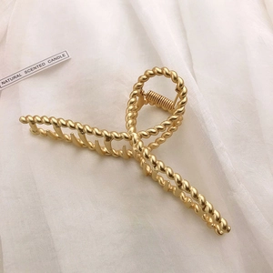 Detail of a large gold metal shark clip featuring a chic woven texture on white fabric