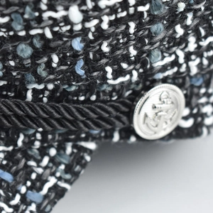 Close-up of tweed wool fabric with a silver anchor button and black braided rope trim