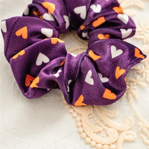 Close-up of purple velvet scrunchie with orange and white hearts on lace background