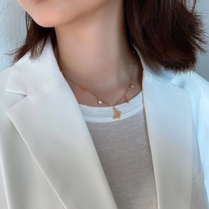 Close-up of golden butterfly necklace with pearl accents on a model in a white blazer