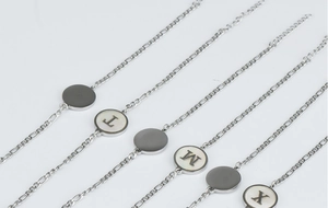 Gros plan de bracelets en acier argenté avec breloques initiales en nacre sur fond gris