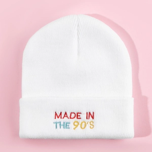 Close-up of MADE IN THE 90'S colorful embroidery on white knit beanie on pink background