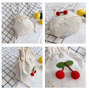 Detail of canvas mini bucket bag featuring embroidered daisies and 3D cherry accents