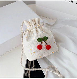 Detail of canvas drawstring bucket bag with daisy embroidery and plush cherry decor