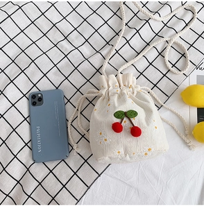 Overhead view of beige canvas bucket bag with cherry decor and daisy embroidery