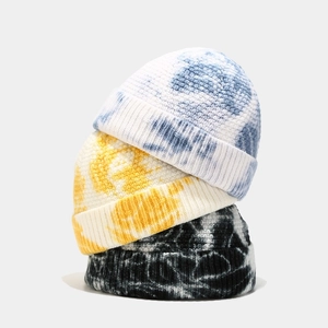 Close-up of three tie-dye knitted docker caps stacked vertically in blue, yellow, and black