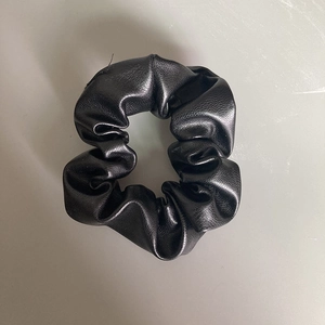 Close-up of black PU leather scrunchie with glossy pleated texture and soft wrinkles