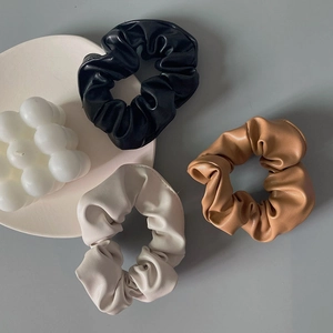 Three premium PU leather scrunchies in black, beige, and brown on a grey background