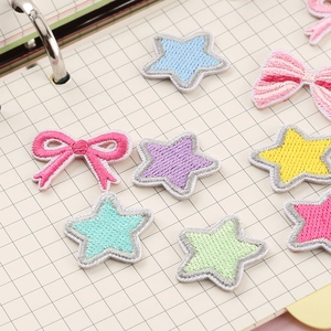 Colorful embroidered star and bow patches in macaron tones on a checkered notebook