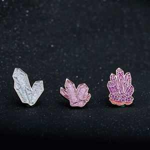 Dettaglio di tre spille in smalto di cristallo glitterato nei toni argento rosa e viola