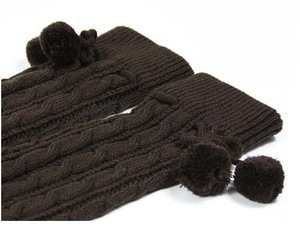 Detail of dark brown cable-knit leg warmers with fluffy pom-poms and textured knit pattern