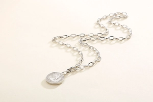 Macro detail of silver stainless steel chain necklace with an embossed coin pendant