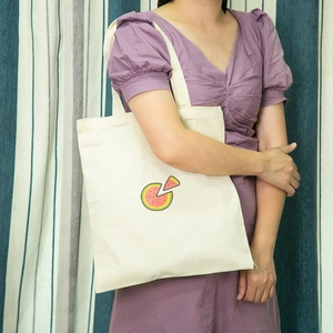 Model wearing an off-white canvas tote bag featuring a fresh watermelon slice print