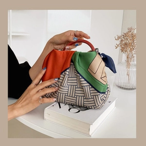 Detail of a chic woven handbag featuring a vibrant geometric patterned silk scarf wrap