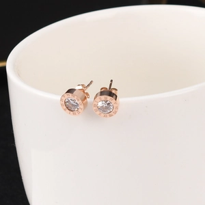 Macro view of rose gold stud earrings featuring roman numerals and a central zircon stone
