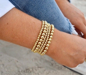 Close-up of five layered 18K gold-plated beaded elastic bracelets on a woman's wrist