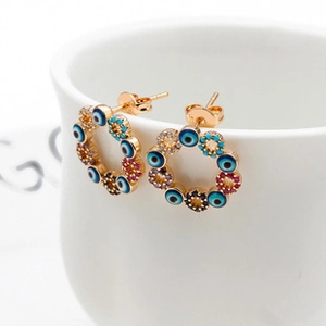 Macro shot of gold-plated evil eye hoop earrings with colorful inlaid crystals on a white rim