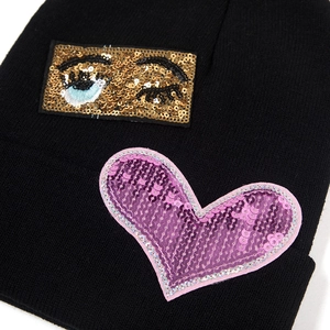 Women's black knit beanie with stylish sequin heart and evil eye patch decorations