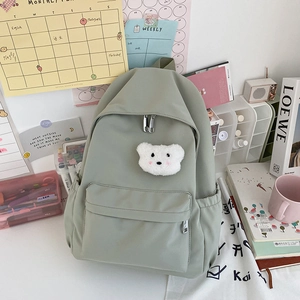 Dettaglio dello zaino verde chiaro minimalista con toppa a forma di orsetto di peluche