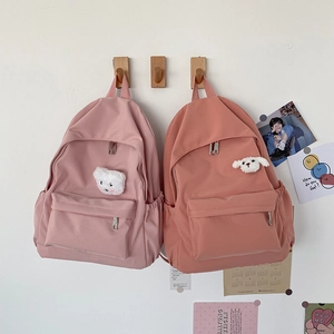 Dettaglio di zaini in nylon rosa con graziosi ciondoli a forma di cucciolo di peluche