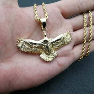 Close-up of a polished gold eagle pendant with a twisted rope chain held in hand
