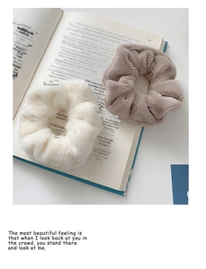 Detail of plush faux fur hair scrunchies in cream and light brown on a book