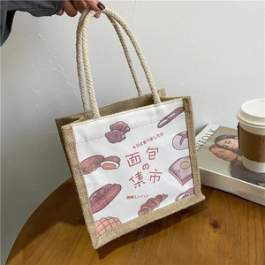 Close-up of canvas lunch bag with bread prints and jute base on a wooden table