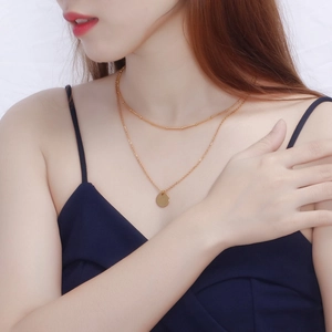 Double-layered gold chain necklace with minimalist round pendant worn on a female neck