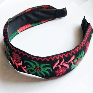 Detail of black fabric headband featuring traditional red and green floral embroidery