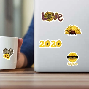 Dettaglio di adesivi girasole impermeabili applicati su laptop e tazza di ceramica