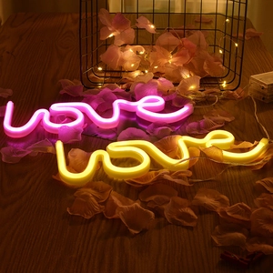 Romantic pink and yellow neon love signs on a wooden table with LED string lights