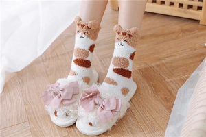 Close-up of fluffy pink slippers with bows and cute cat patterns on cozy coral fleece socks