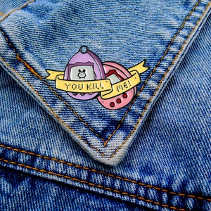 Dettaglio di spille in smalto stile Tamagotchi su denim con testo You Kill Me